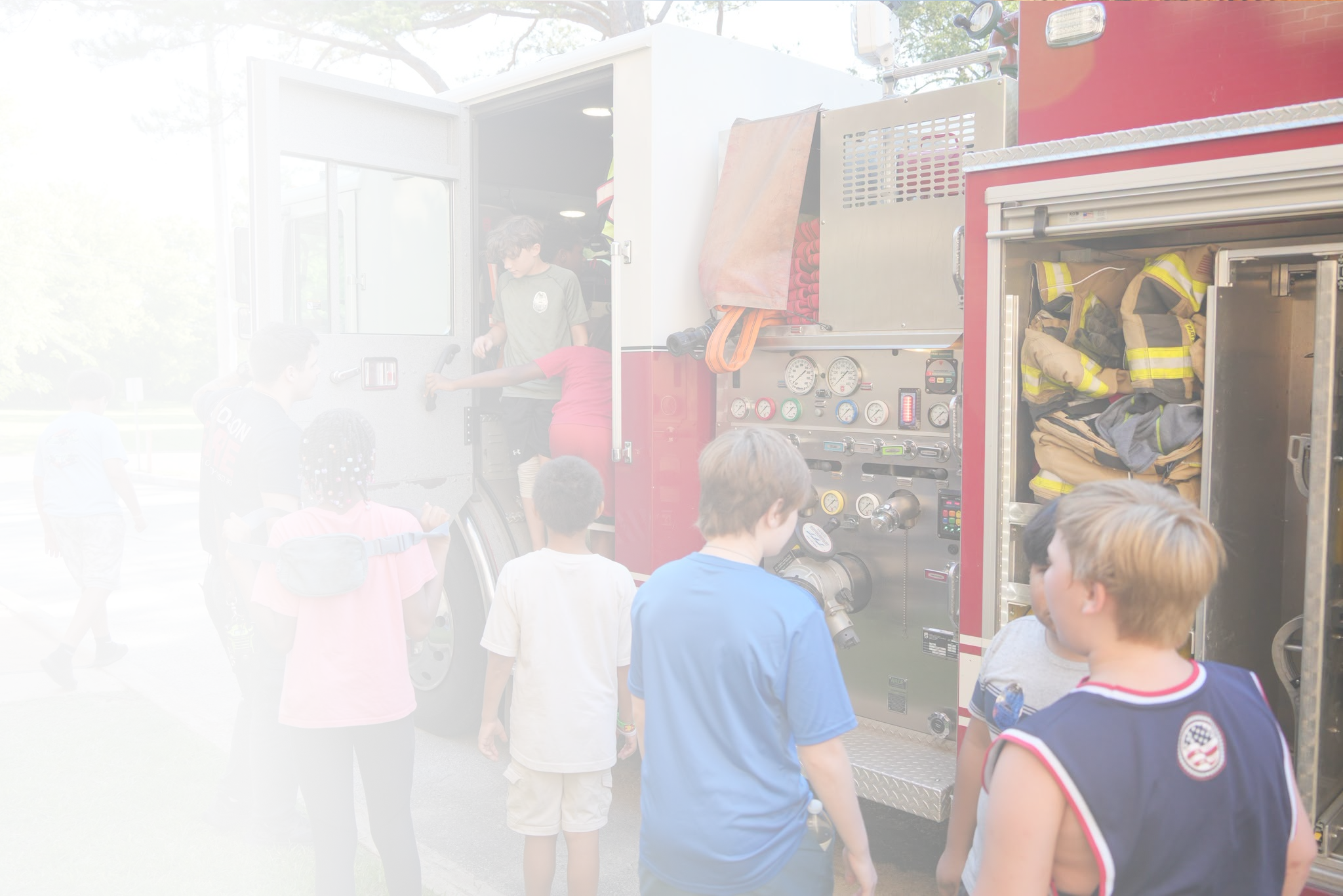 Children gathered around a fire truck, observing its equipment and interior during a community safety event.