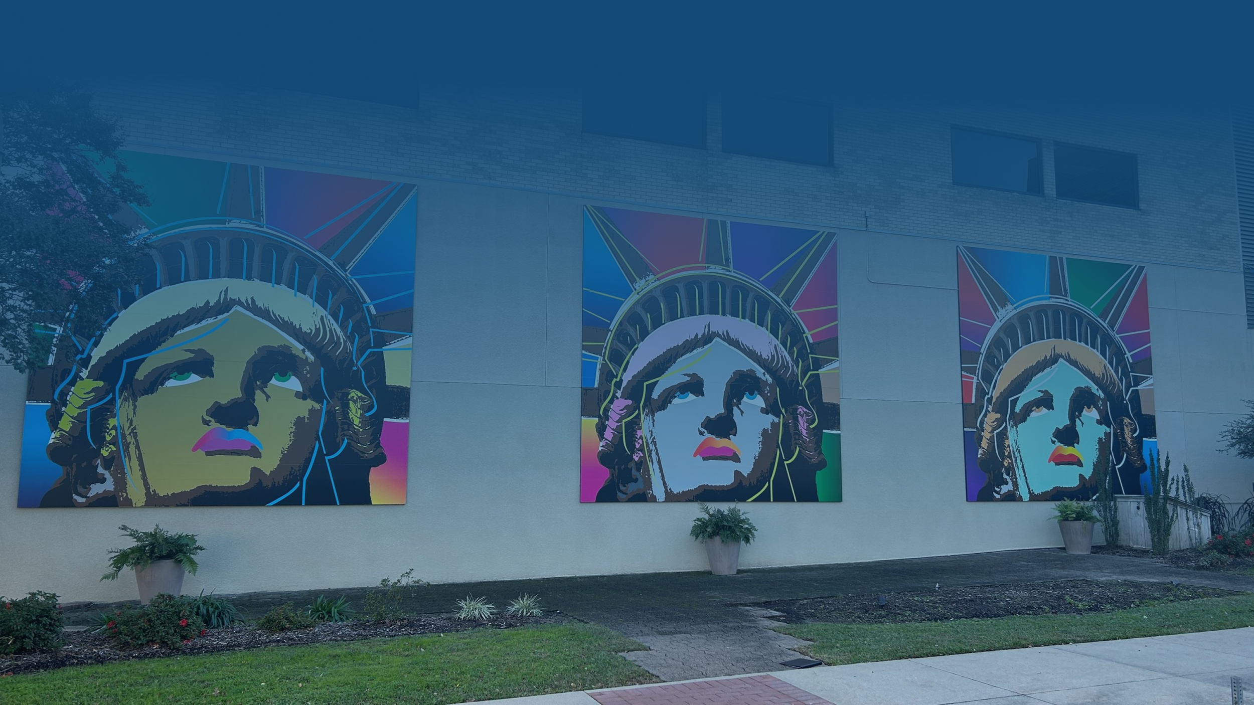 Three large colorful murals of the Statue of Liberty on an exterior wall of a building.