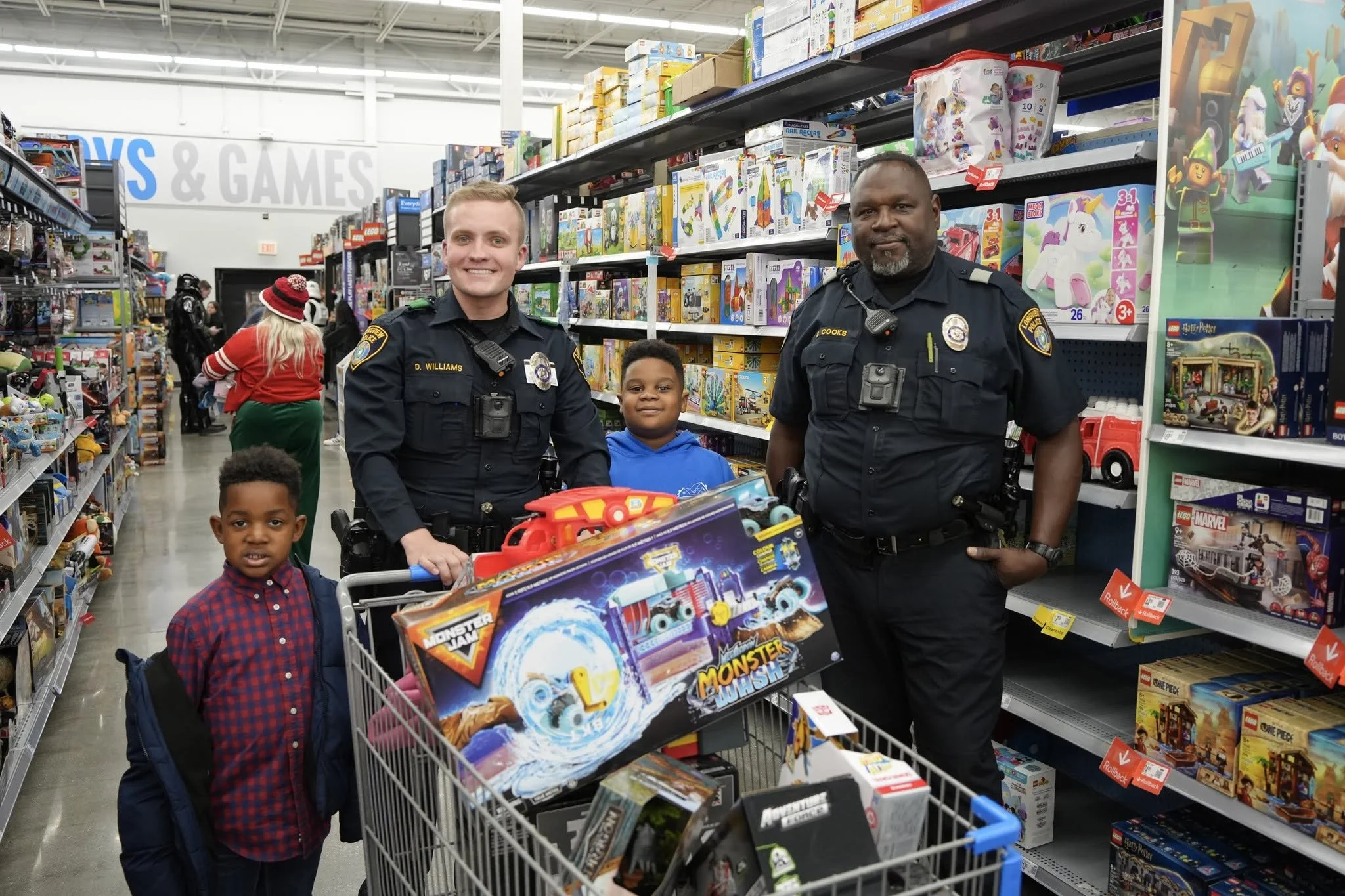 Two police officers and three children in a toy store aisle filled with toys and games, shopping for toys.