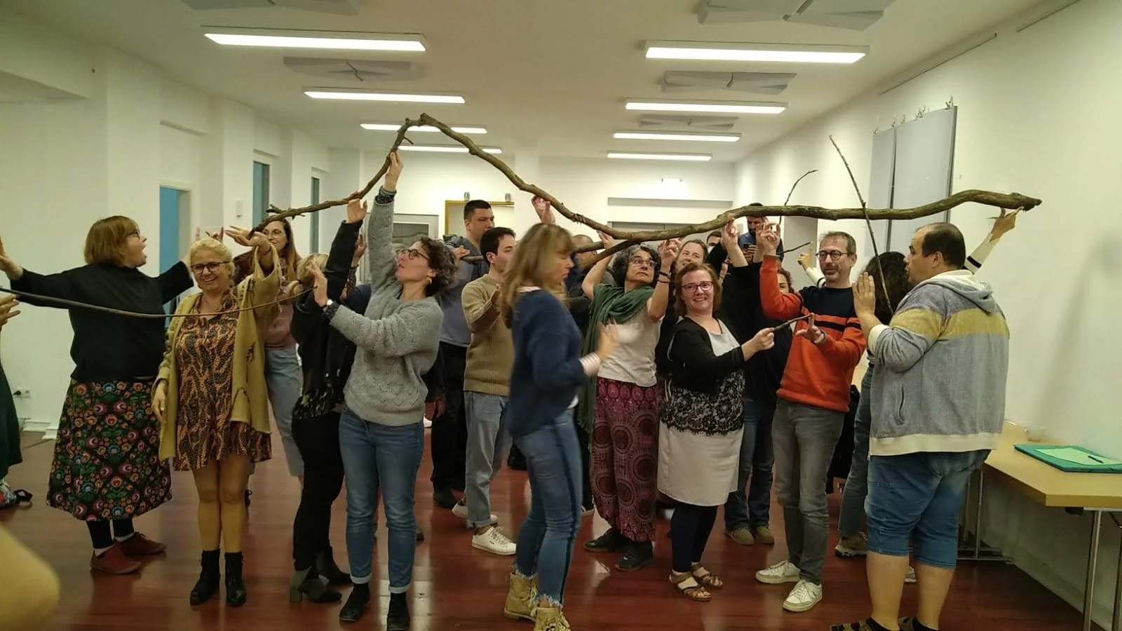 Menschen in einem Raum, die gemeinsam einen langen Baumstamm halten, vermutlich bei einer Gruppenspielaktivität.