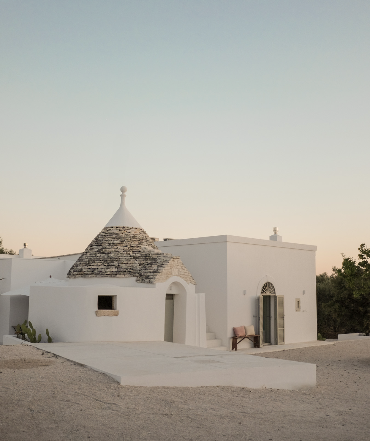 White Mediterranean-style building with a cone-shaped roof made of stone, set against a clear sky at dusk.
