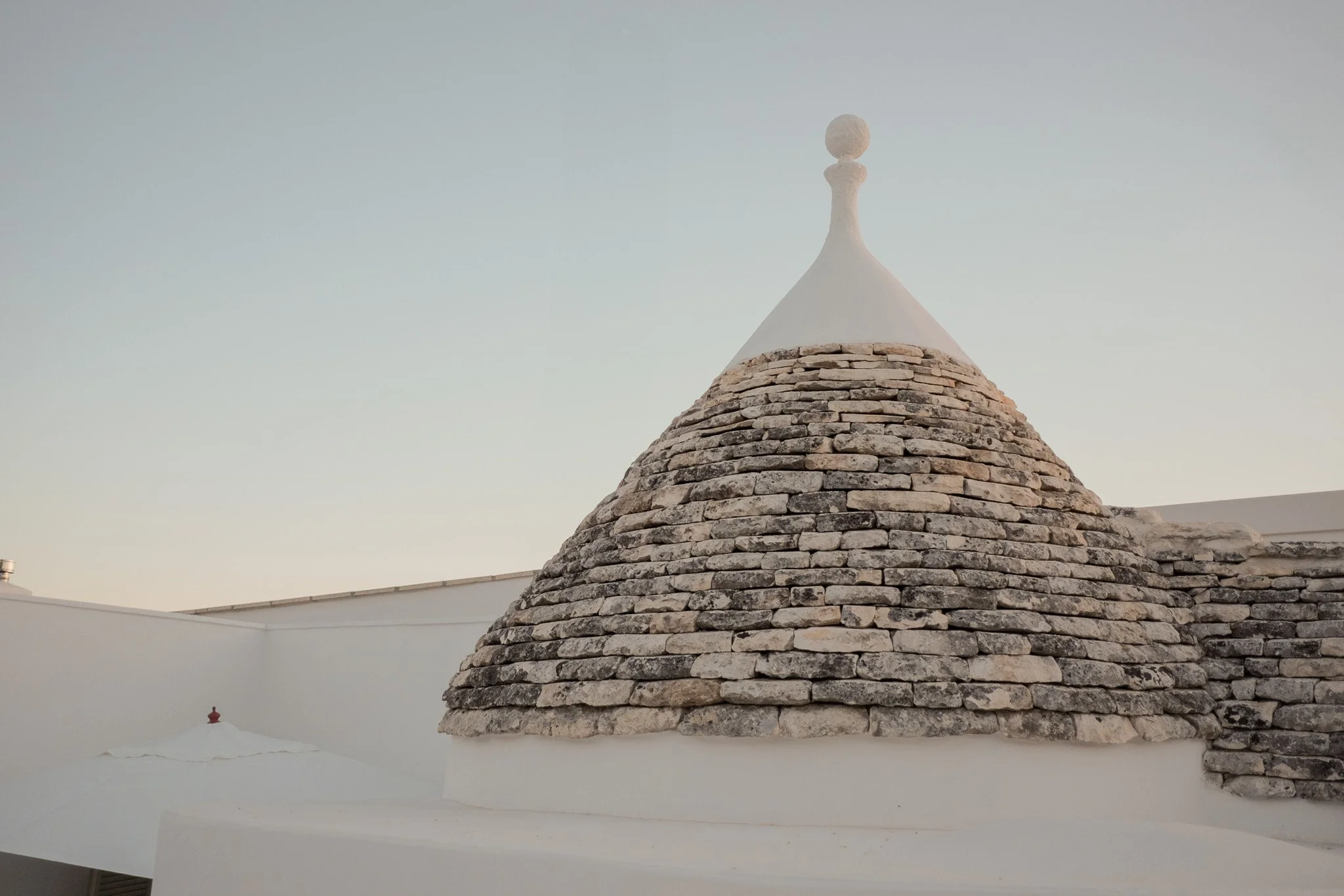 A stone roof with a conical shape and a decorative white top, against a clear sky.