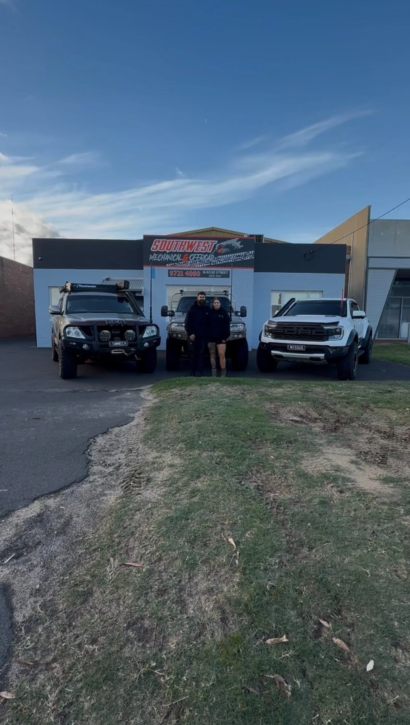 Two men and one woman standing in front of three Toyota Land Cruiser off-road vehicles outside a building with a sign for Southwest Mechanical & Offroad.