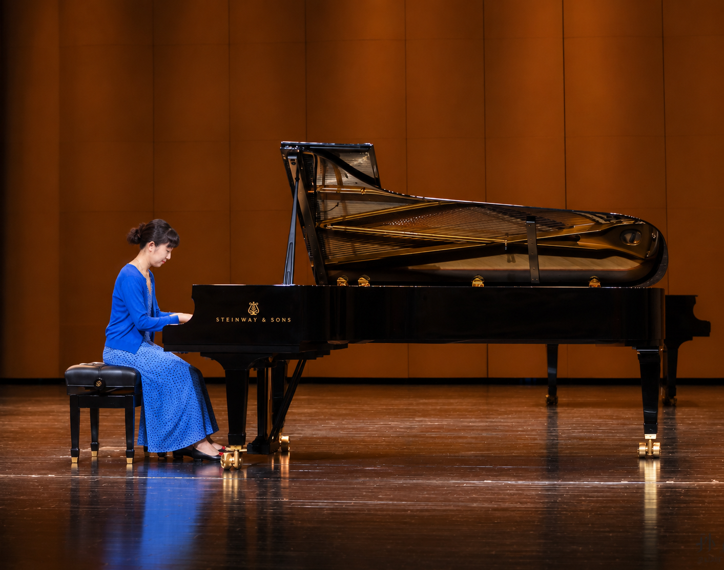 Pianist in a blue dress playing a Steinway grand piano on a concert hall stage.