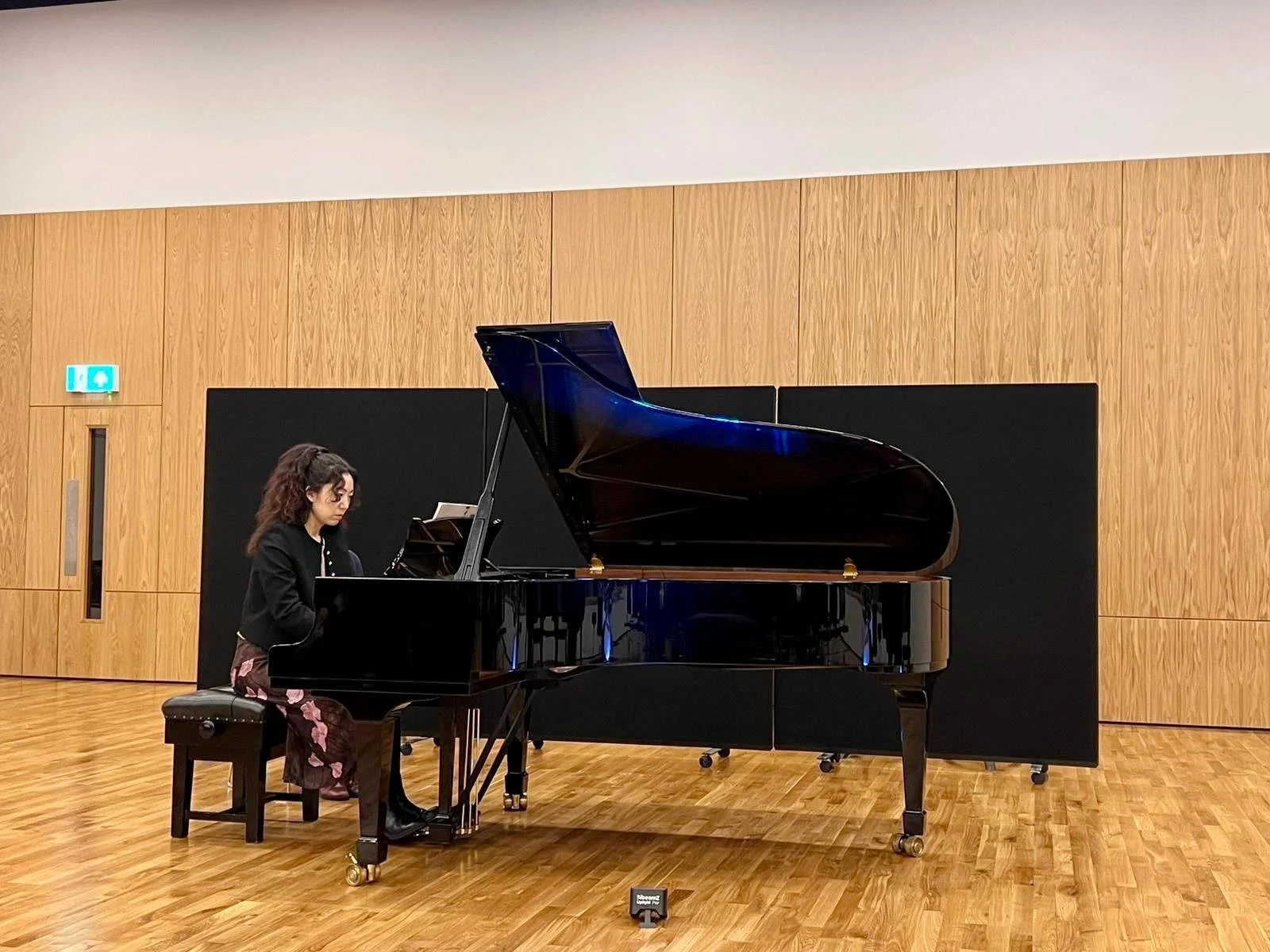Woman playing a black grand piano in a wood-paneled concert hall