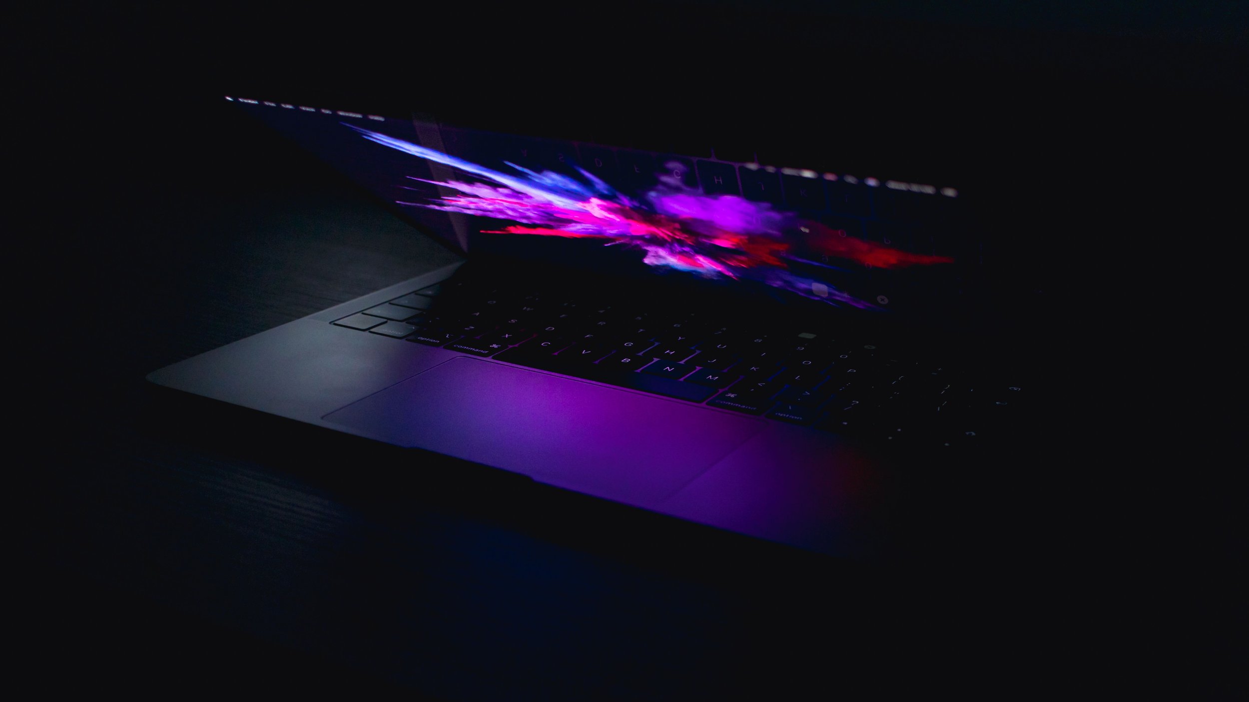 A laptop with a colorful, abstract screen display in a dark room.