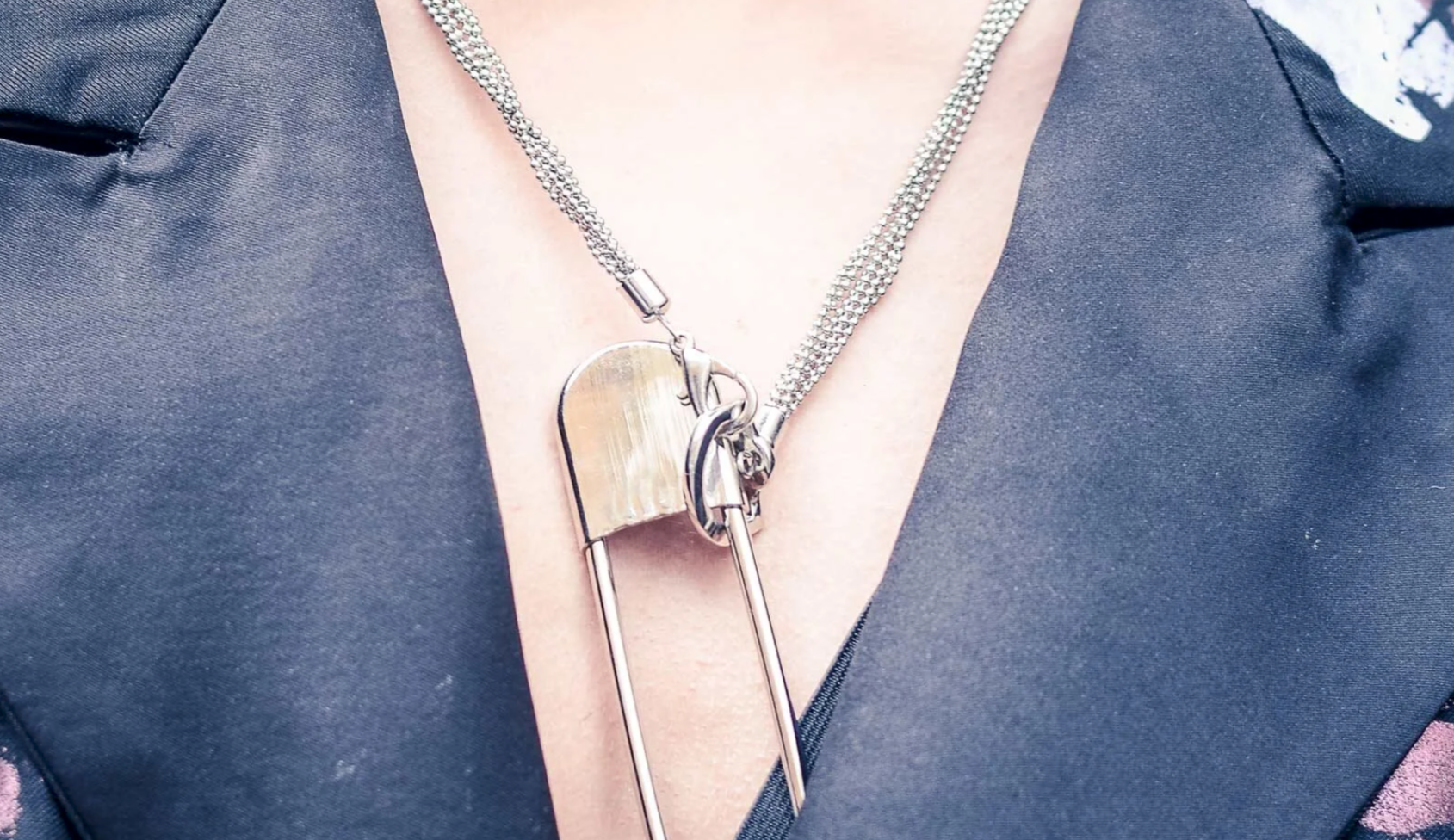 Close-up of a person wearing a silver chain necklace with a large safety pin pendant.