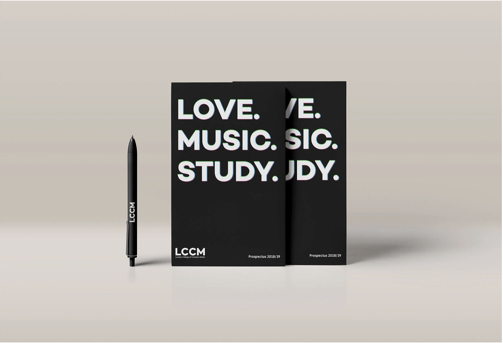 Black pen with white text saying "LCCM" next to two black booklets with the words "LOVE. MUSIC. STUDY. JDY." in white and green letters. The booklet also has "LONDON COLLEGE OF CREATIVE MEDIA" and "Prospectus 2018/19" printed at the bottom.