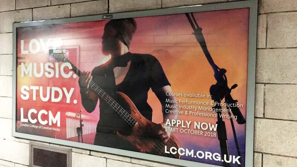 An advertisement featuring a woman with a head wrap playing an acoustic guitar in a music studio or classroom environment.
