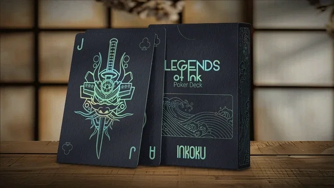 Two black playing cards and a box labeled 'Legends of Ink Poker Deck' on a wooden surface.