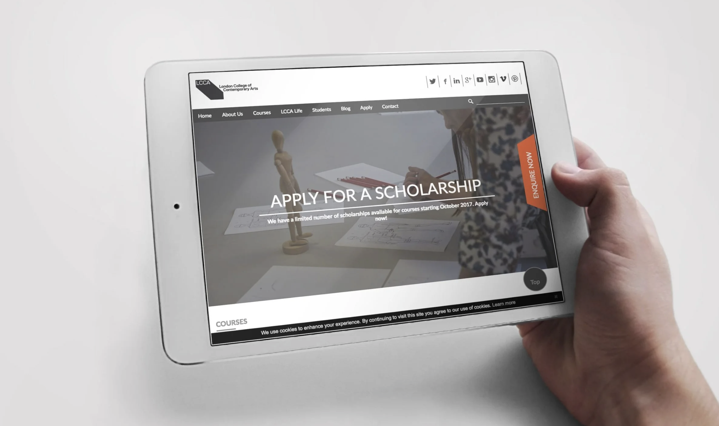 A person holding a white tablet displaying a webpage from London College of Contemporary Arts with an application for a scholarship, featuring images of a wooden mannequin and sketches.