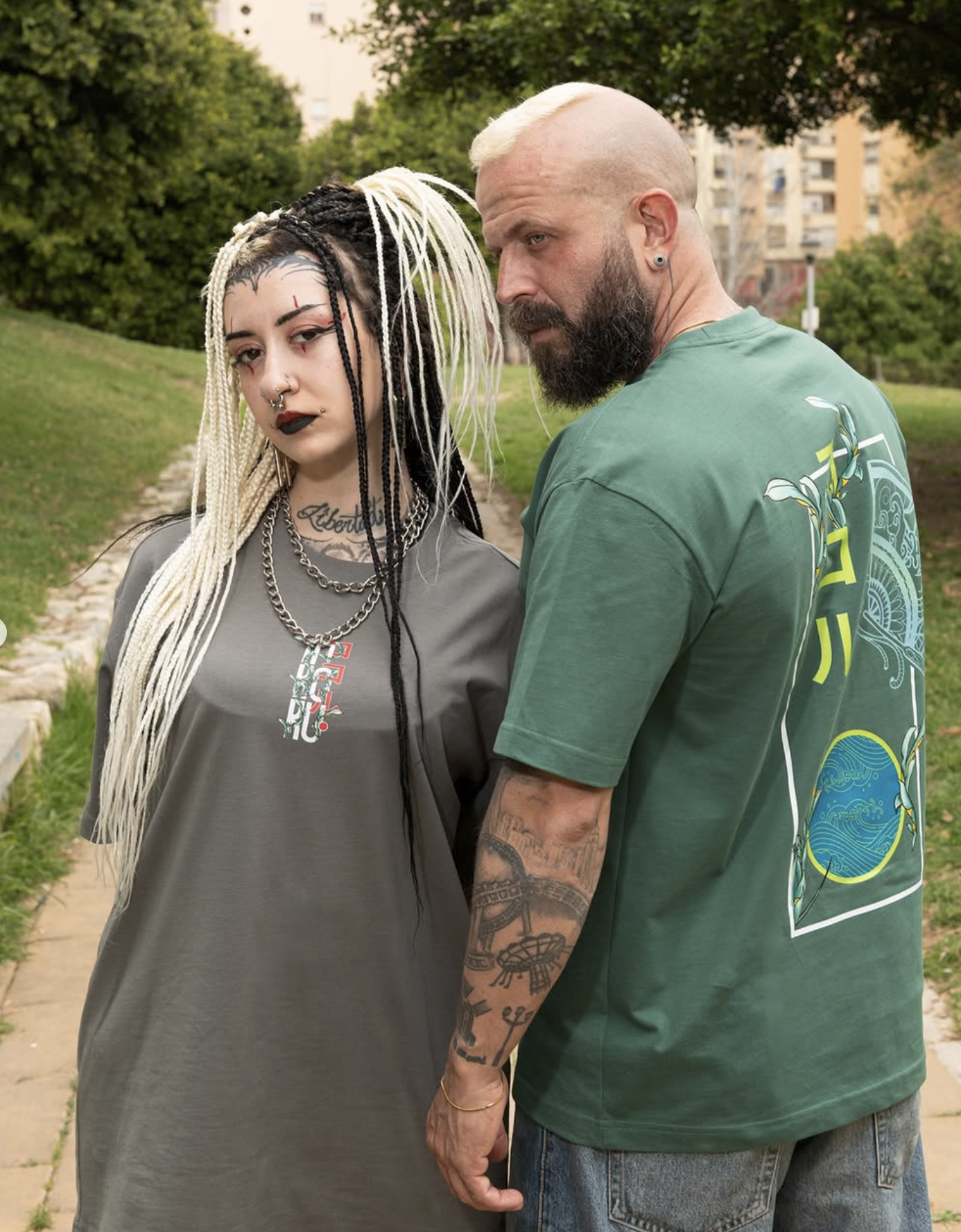 A young woman and a man standing close outdoors, holding hands, with trees and apartment buildings in the background.