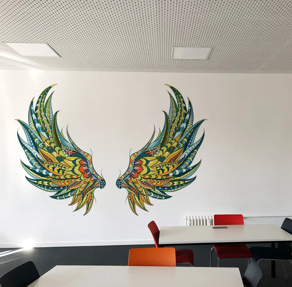 Colorful mural of two symmetrical phoenixes with intricate feather designs on a plain white wall, in a room with tables and chairs.