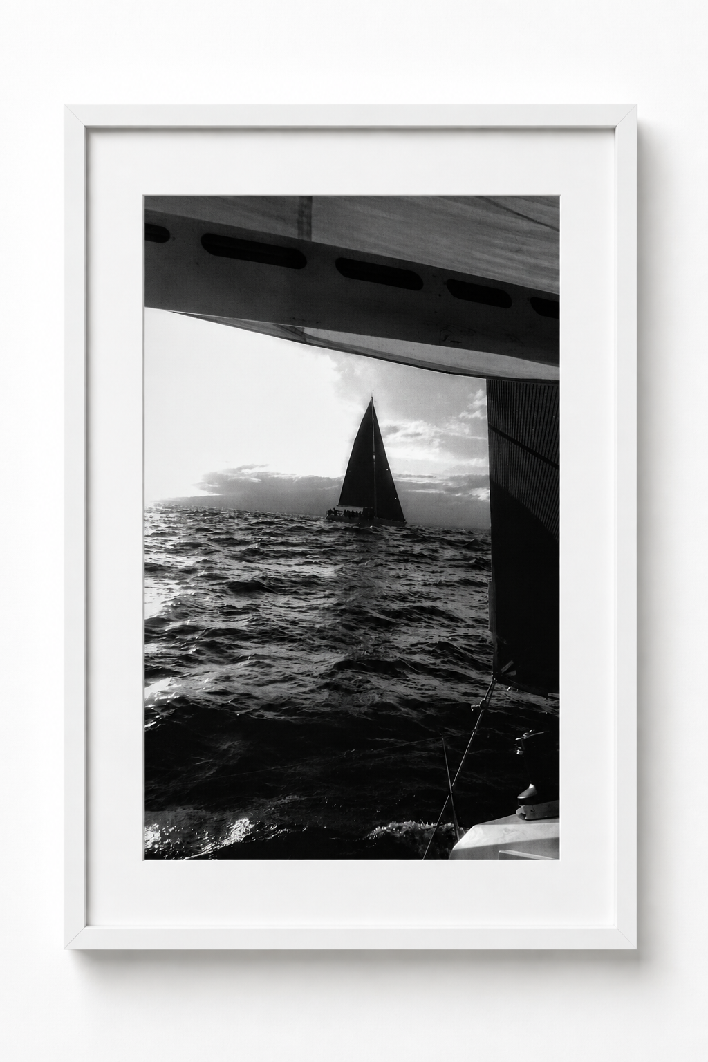 Found at Sea, a white-framed black and white photograph of a dark sailboat viewed beneath the edge of another vessel. Fine art photography prints by Terron Studio.