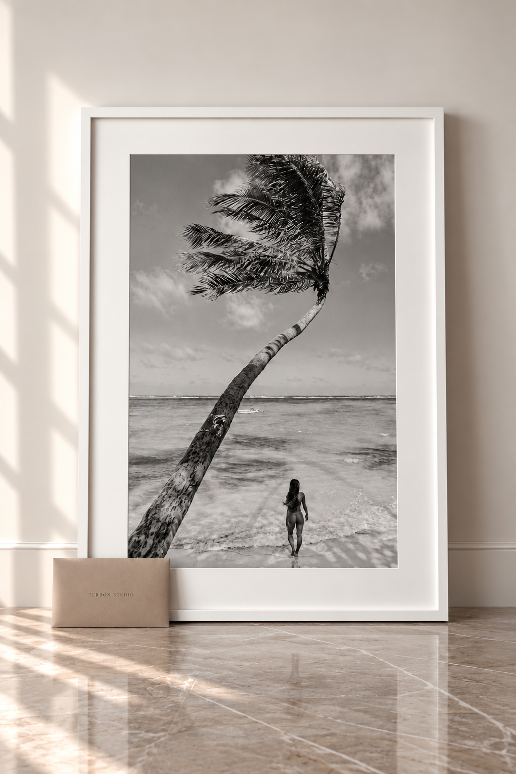Anywhere You Go, a beach figure beneath a windswept palm, in a white frame leaning against a wall. Fine art photography prints by Terron Studio.