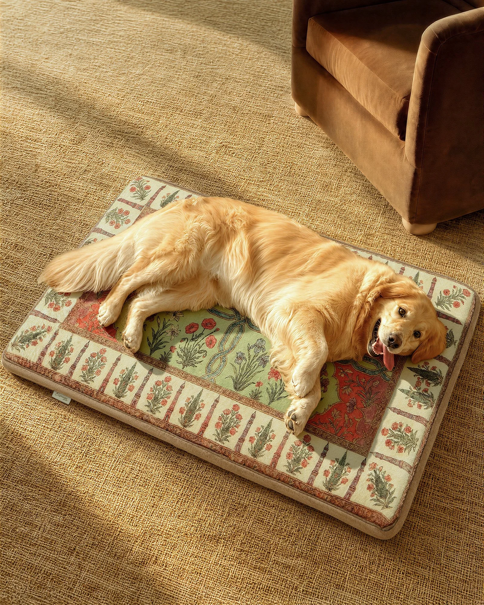A golden retriever lying on a decorative dog bed on a textured beige carpet, near a dark brown armchair.