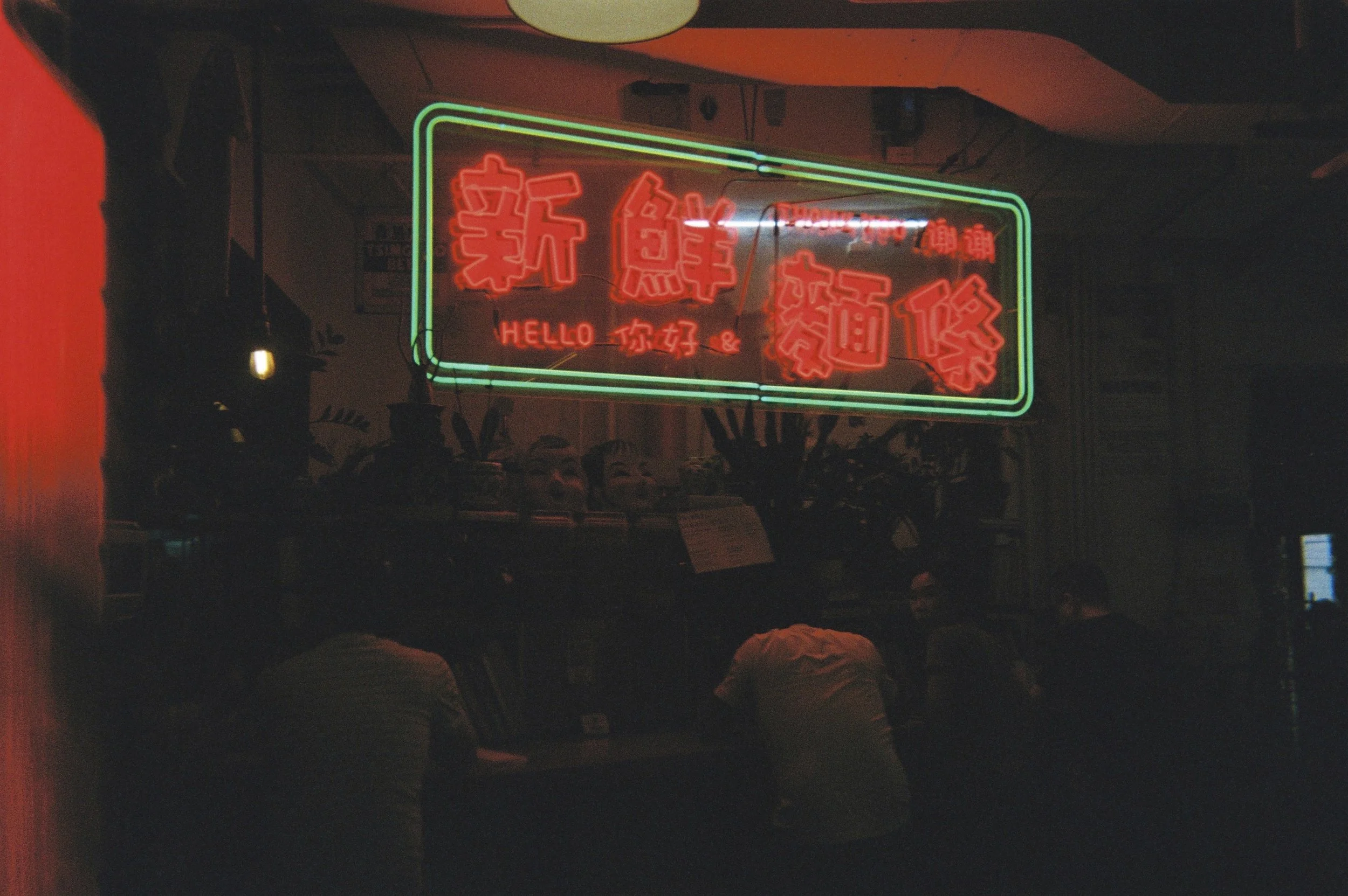 Neon sign with red and green Chinese characters and the words 'HELLO' and '你好' in red, hanging inside a dimly lit establishment.