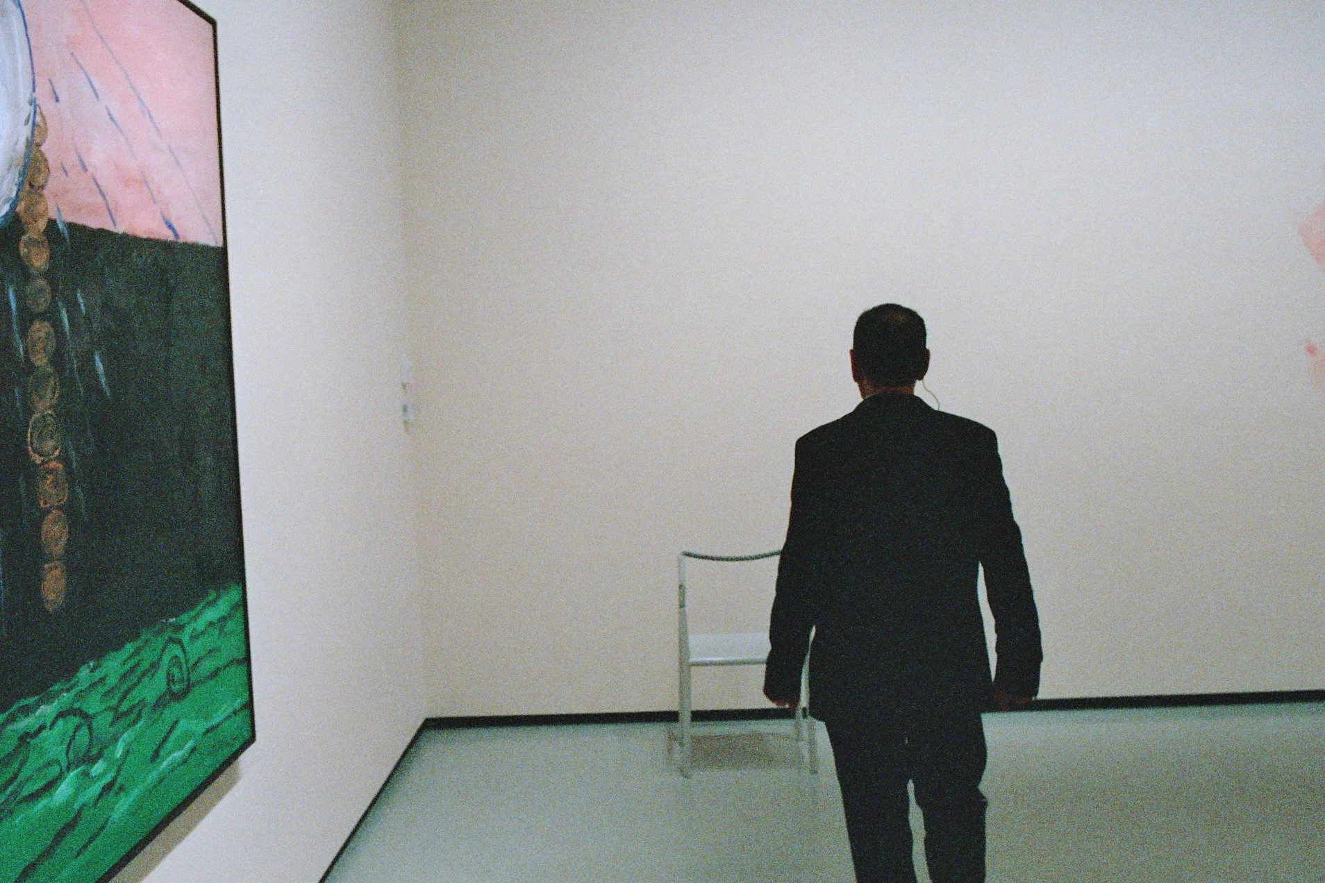A museum guard in a black suit walking through an art gallery with white walls, looking at the artworks displayed.
