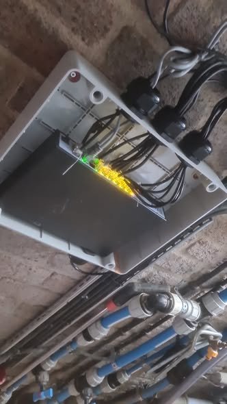 Electrical panel with wires connected, mounted on a wall above plumbing pipes.