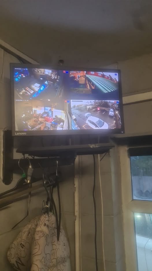 A security monitor showing multiple camera feeds of indoor and outdoor areas, mounted above a window with hanging items below.