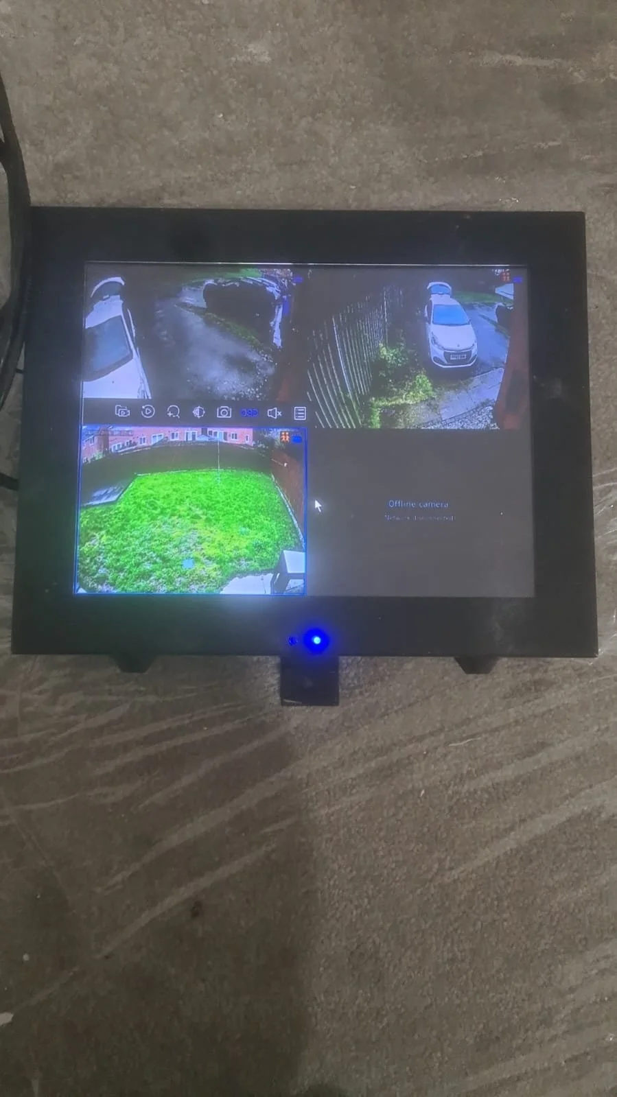 Security monitor displaying four camera feeds, showing parking lot and yard area, with various icons and settings at the top.