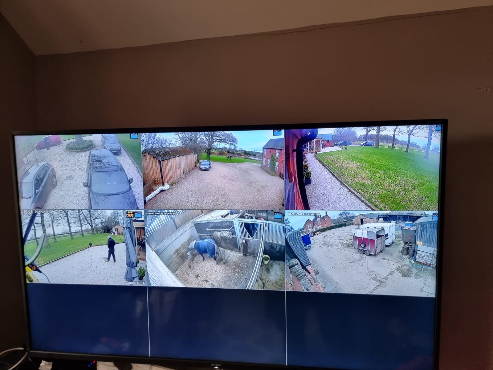 Multiple security camera feeds showing various outdoor and indoor scenes, including parked cars, a person walking, a horse in a stable, and buildings on a farm or rural property.