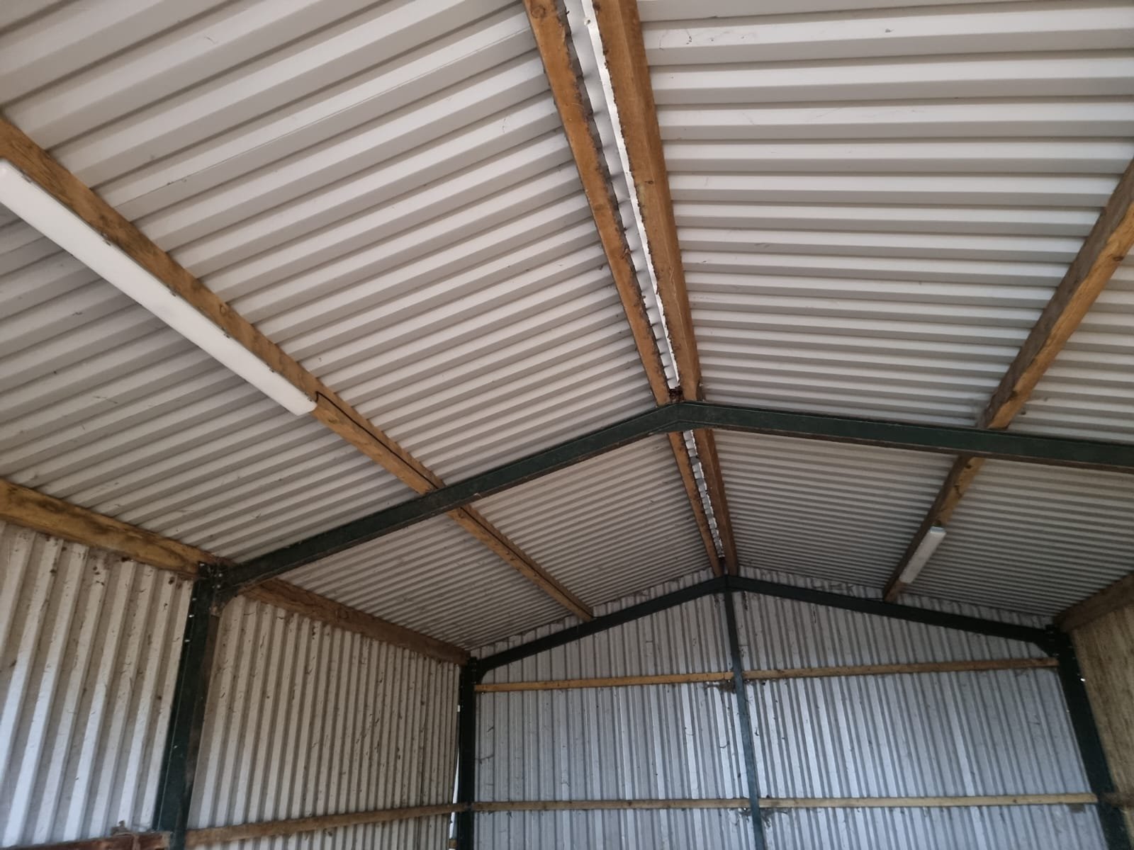 Interior view of a metal building with corrugated metal walls and ceiling, supported by wooden beams and metal framing.