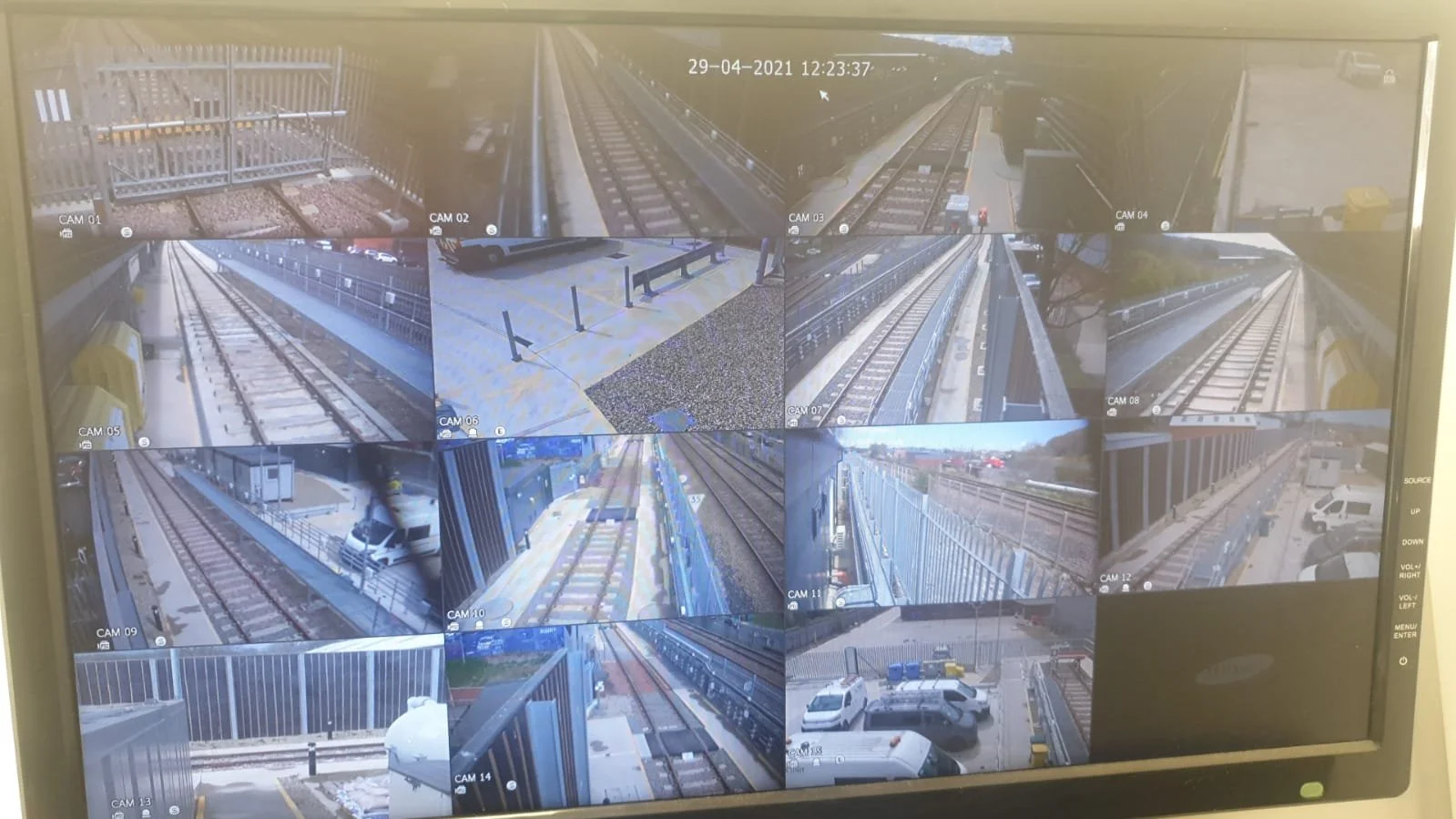 Multiple surveillance camera feeds showing various views of train tracks, a parking lot, and a fence at a train station.