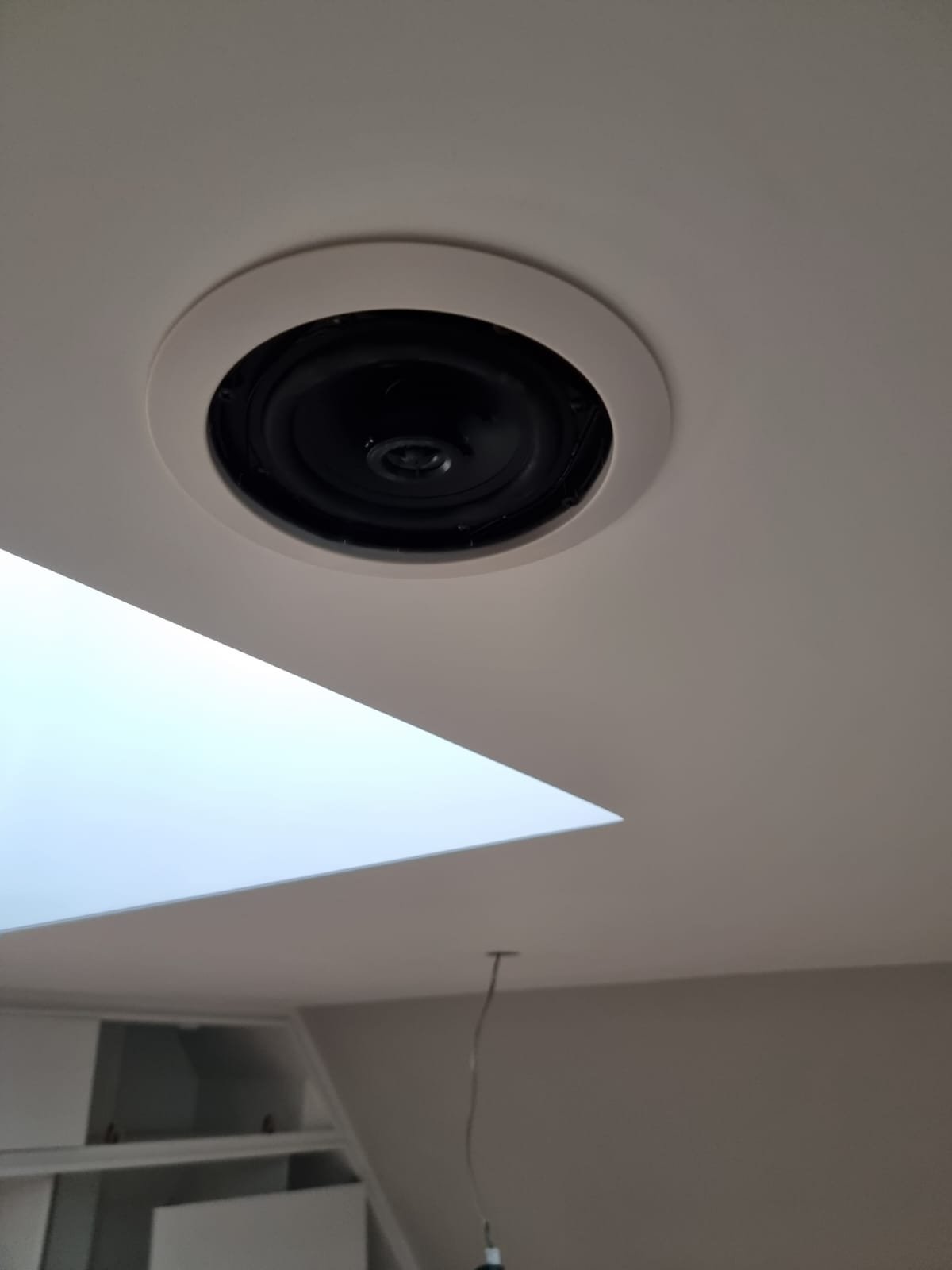 Ceiling with a black recessed speaker and a square skylight in a room.