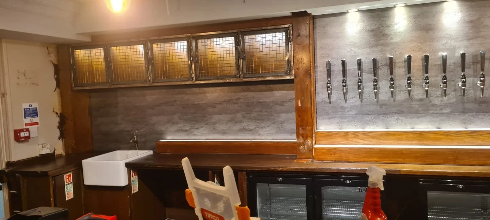 Wall with metal knives displayed and a small sink in a rustic kitchen or bar area.