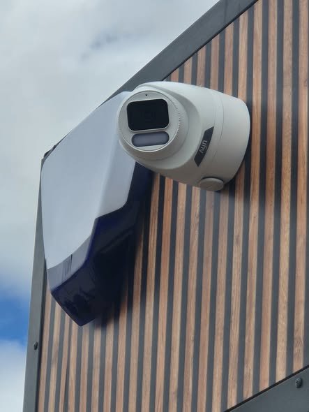 A close-up view of an outdoor security camera mounted on a wall near a railing.