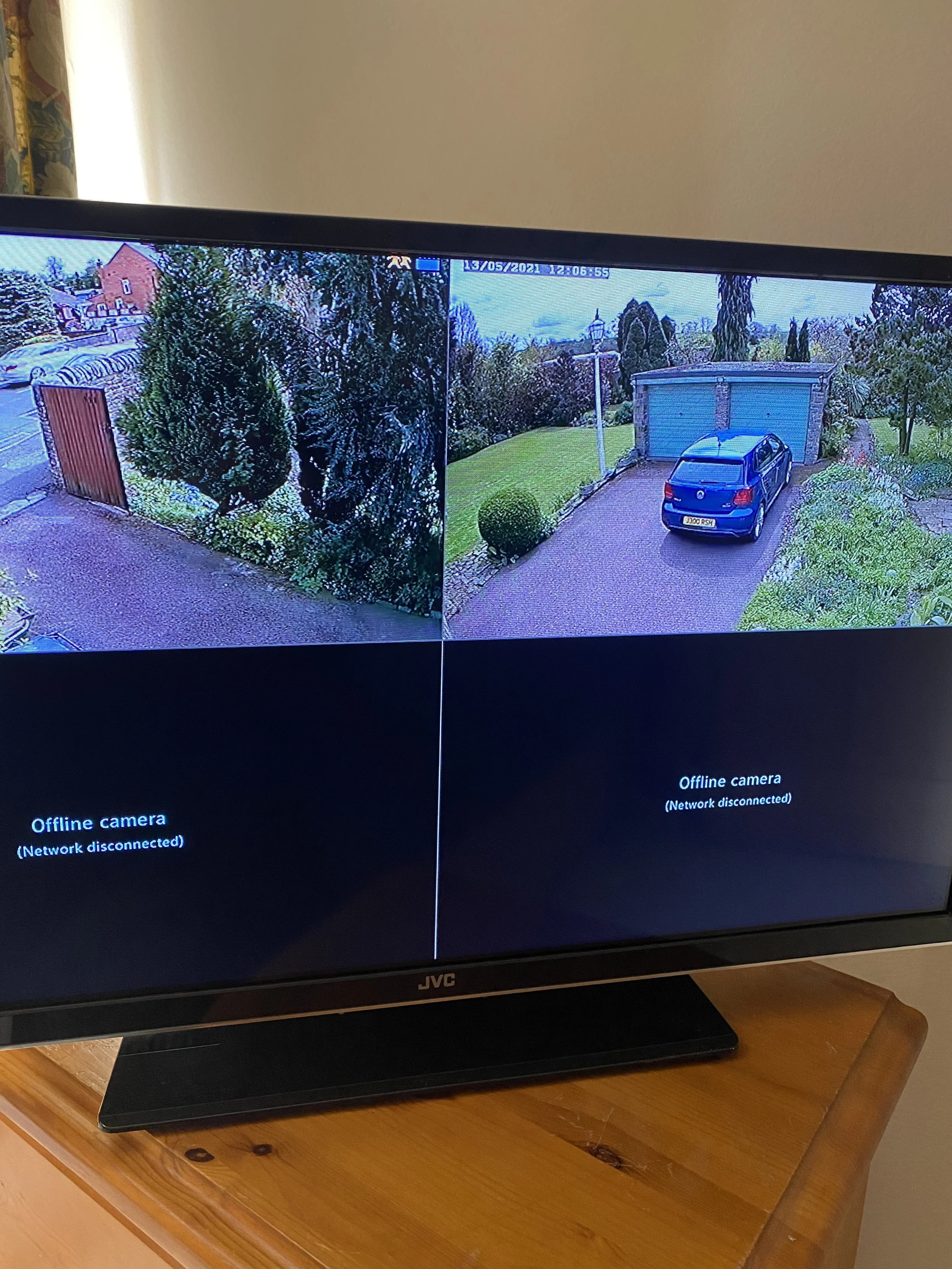 A split-screen security monitor on a wooden table, showing two outdoor surveillance camera feeds with the message 'Offline camera (Network disconnected)' at the bottom of both screens.