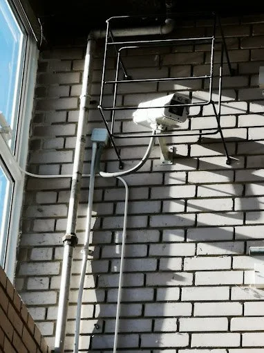 Security camera mounted on a brick wall near a window with a metal rack above it.