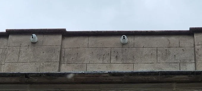 Two security cameras mounted on the side of a building under an overcast sky.