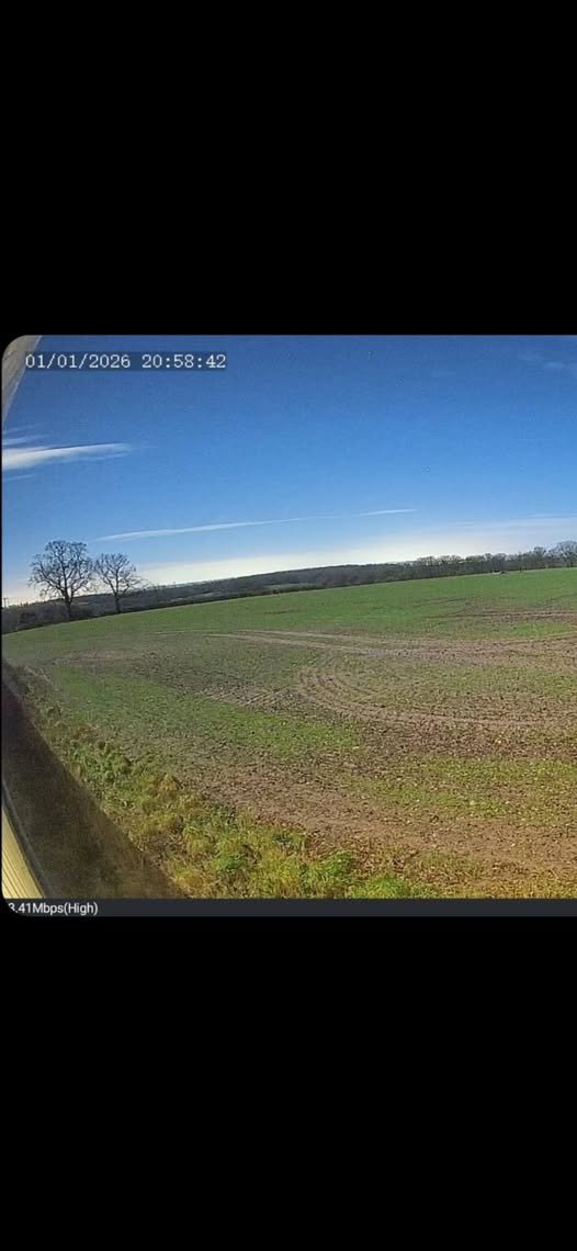 A rural landscape with open fields and sparse trees under a blue sky with a few clouds.