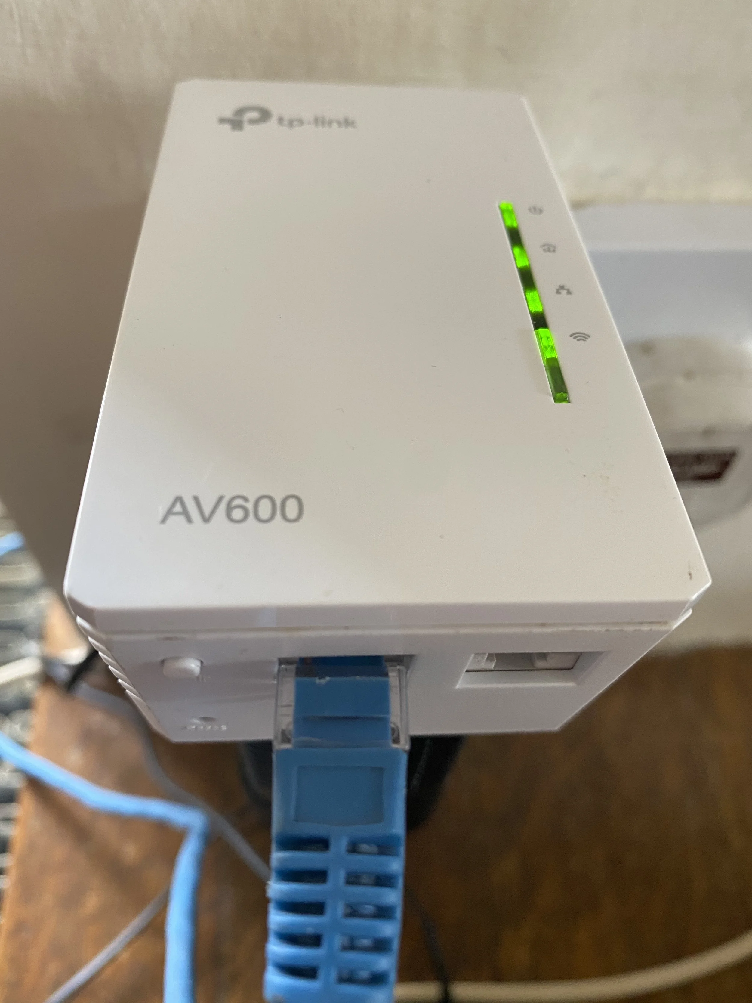 Close-up of a white AV600 Powerline Adapter with LED indicators showing power, data, Ethernet, and Wi-Fi, connected via a blue Ethernet cable.