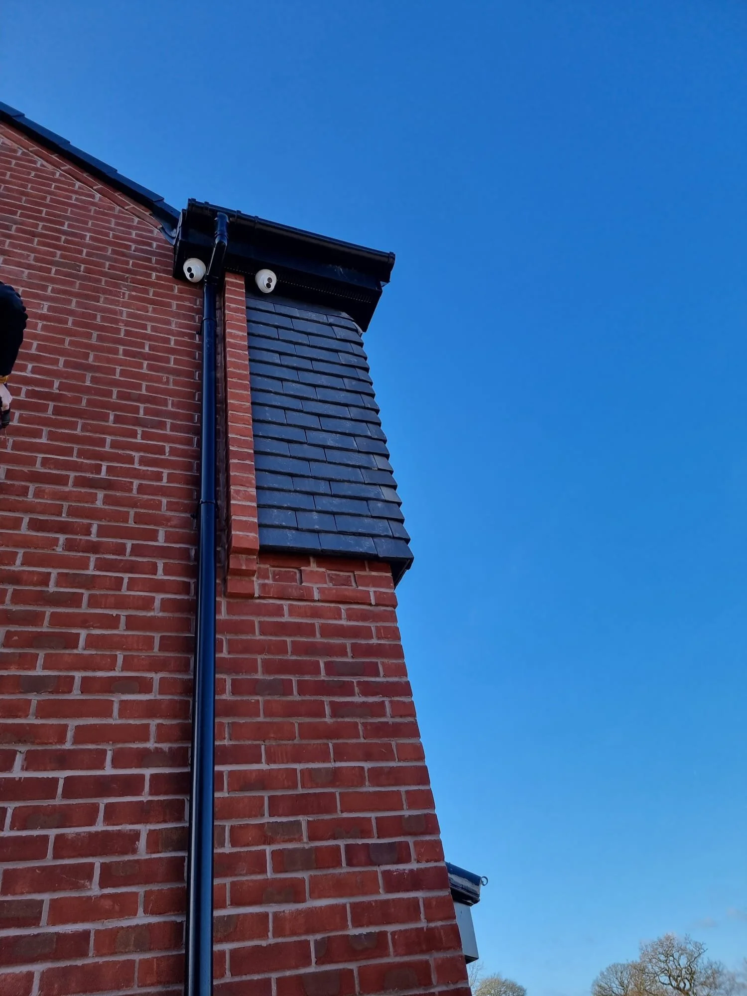 Close-up view of a brick house corner with a black gutter and downspout, and a clear blue sky in the background.