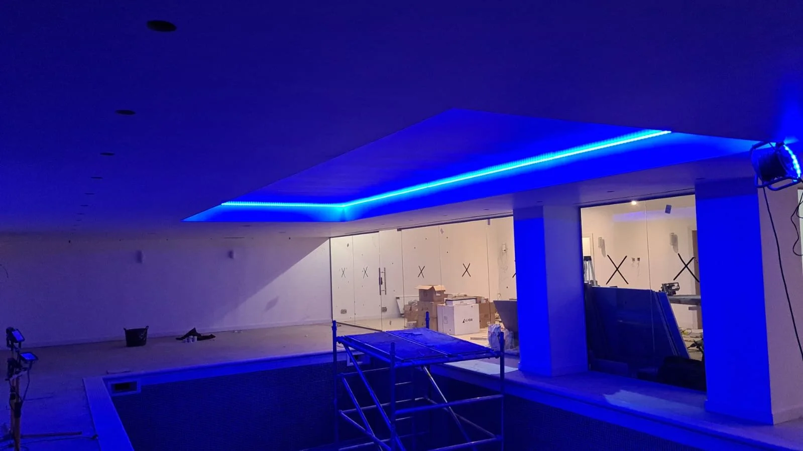 Indoor swimming pool under construction with blue LED lighting along the ceiling.
