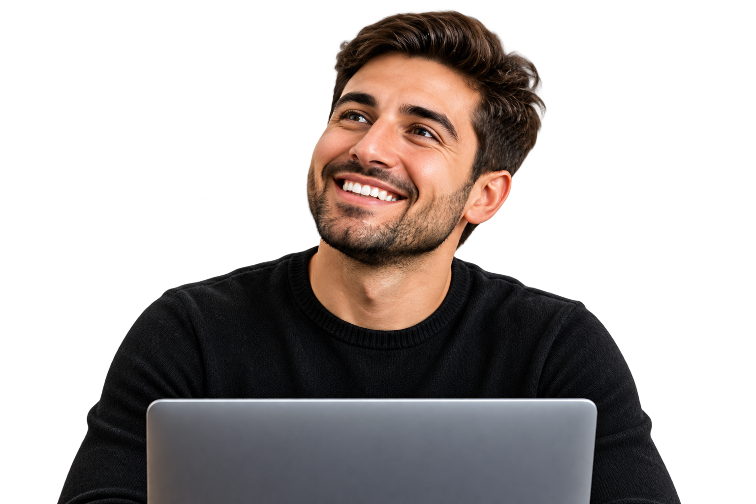 A young man with dark hair and a beard, smiling and looking upward, sitting in front of a laptop.