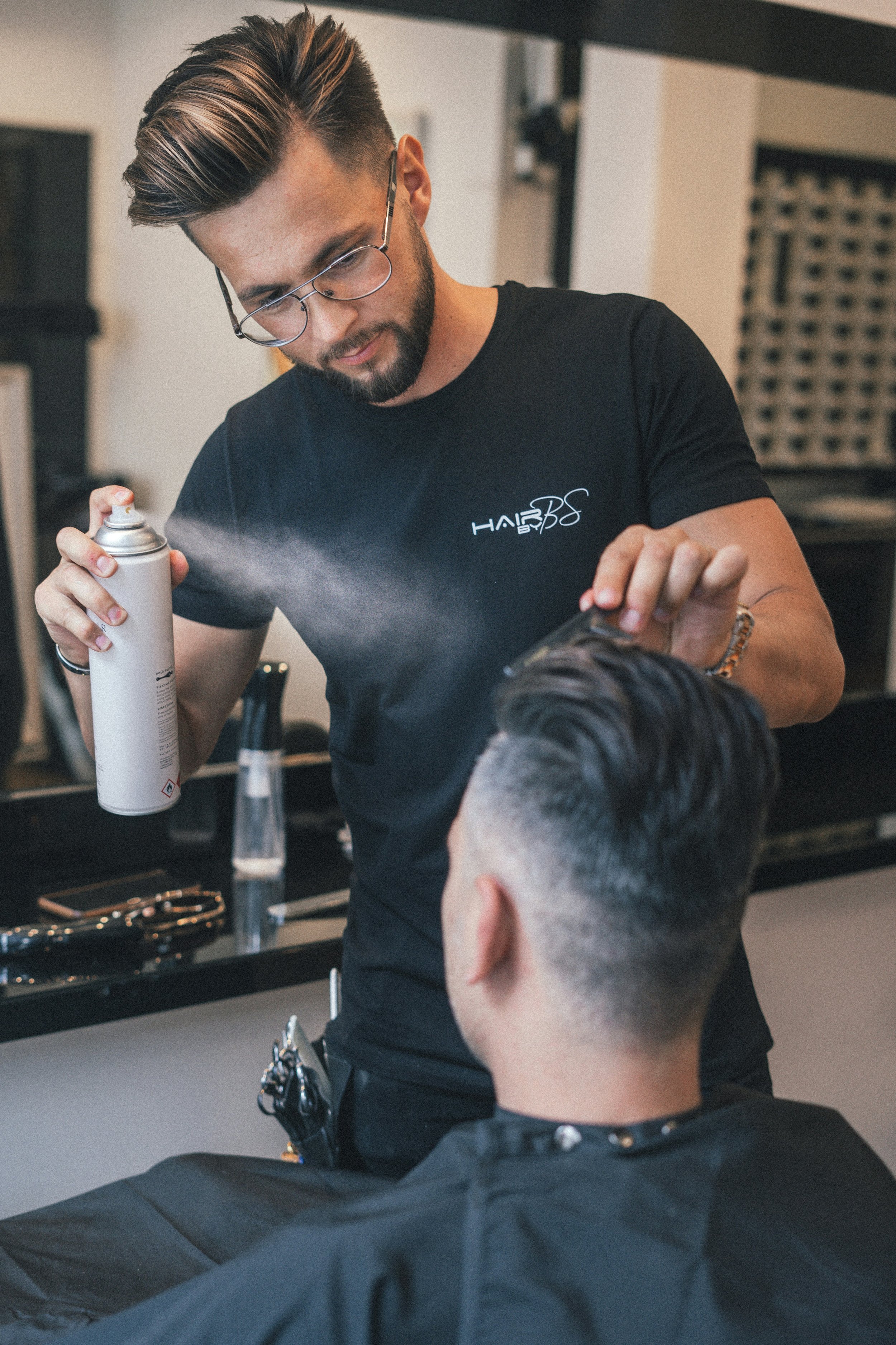 A hairstylist applying hair spray on a client’s hair in a salon.