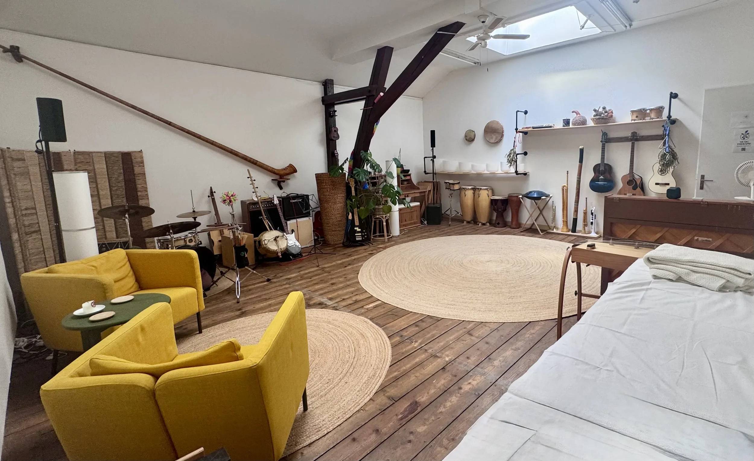 Gemütliches Wohnzimmer mit Musikinstrumenten, Musikanlage, Pflanzen, gelben Sessel, Teppichen, Bett, und Dachfenster im Dachboden.
