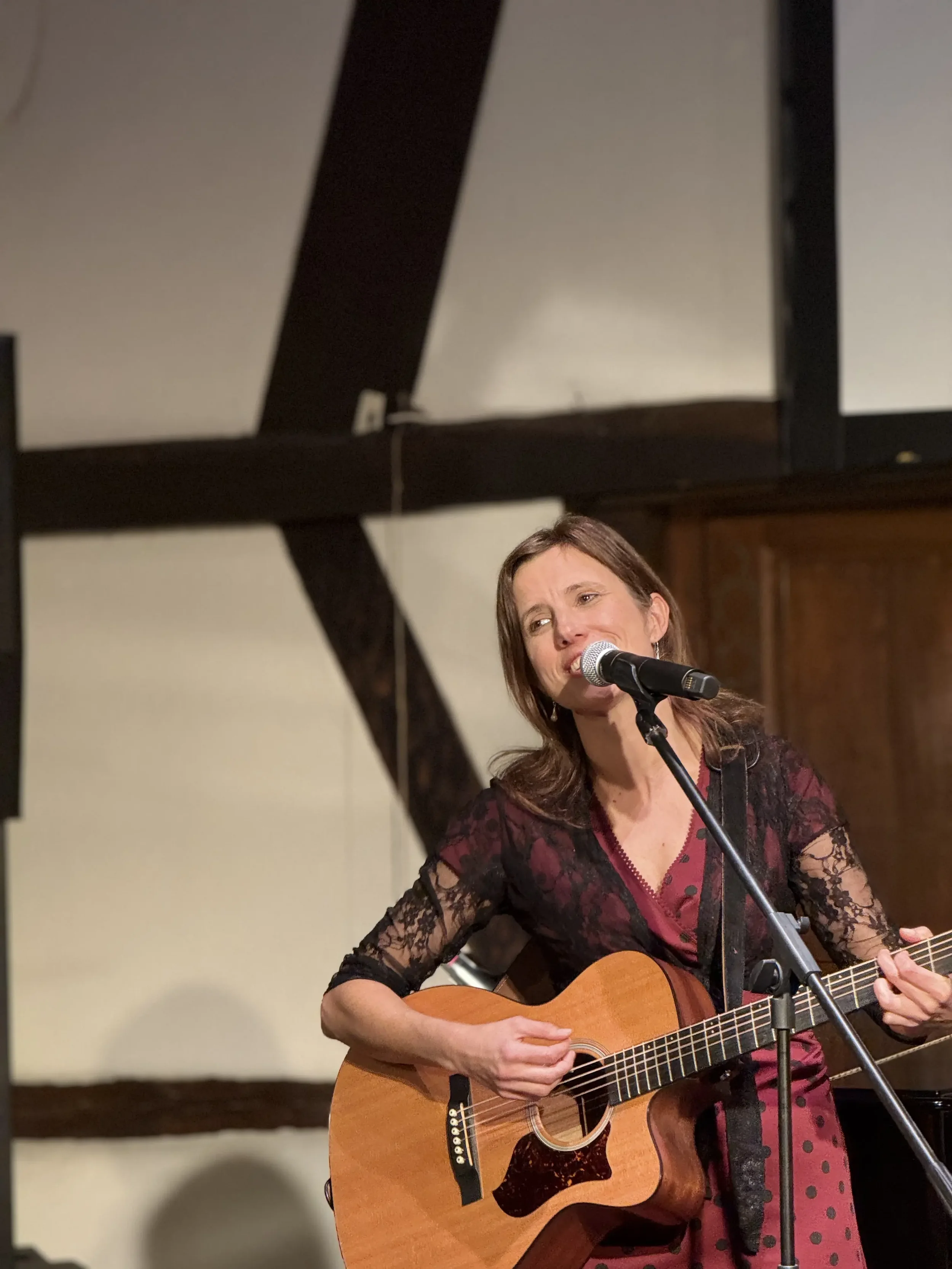 Sereina Ueberwasser, Inhaberin Overwater Musiktherapie in 4410 Liestal Basel-Land, singt und spielt Gitarre an einem Mikrofon in einem Raum mit Holzmöbeln