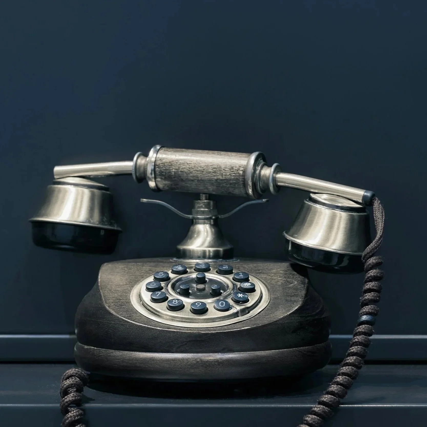 Gammelt telefon med skruer og mekanisk kobling på en sort baggrund.
