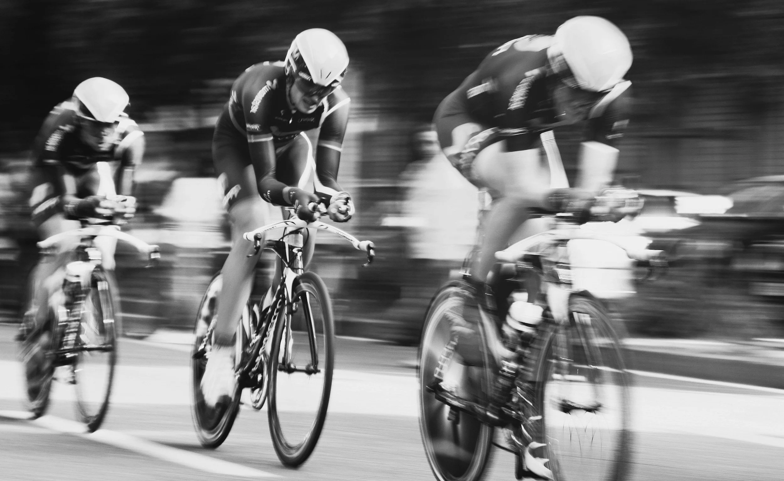 Sort-hvid billede af tre cyklister, der racer på en vej, i høj hastighed, med bevægelseseffekt.