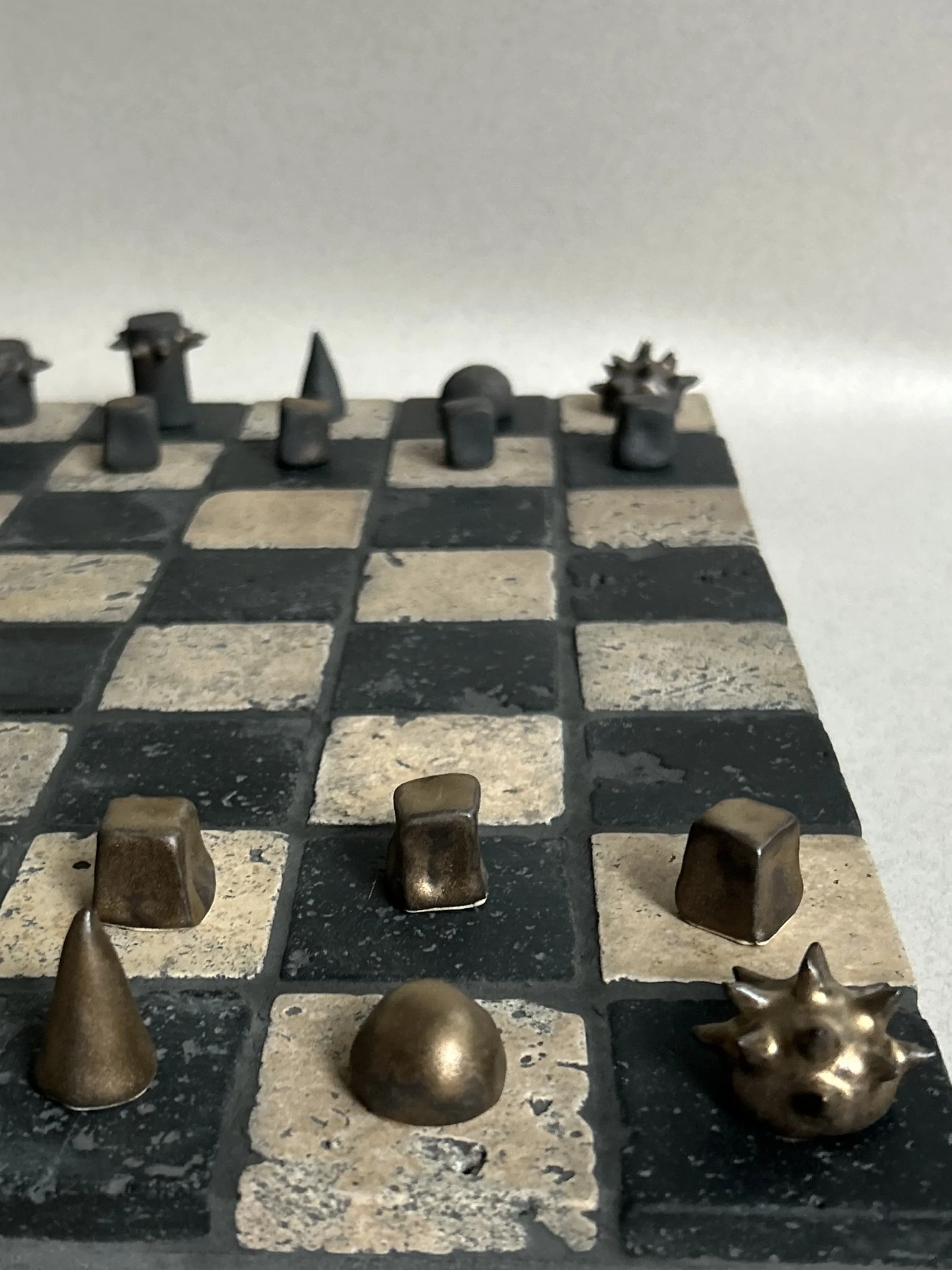 Close-up of a vintage chessboard with worn, metallic chess pieces on black and white squares. The focus is on the lower right corner with a lion head chess piece in the foreground.