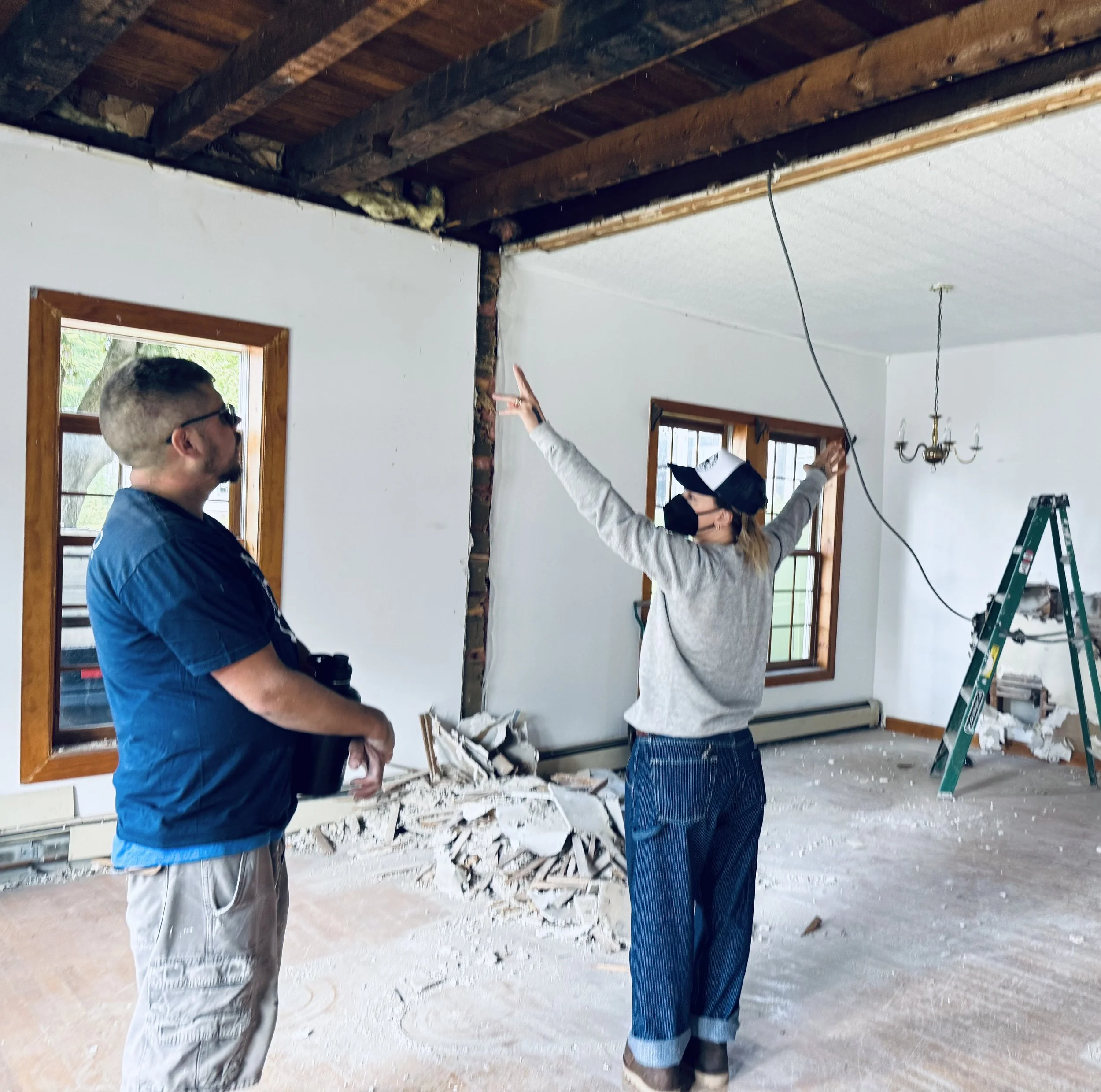 Two people inspecting a construction site, looking at the ceiling where insulation and framing are visible, with one person pointing at the ceiling and the other observing.