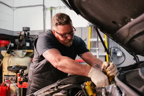 A man working on a car engine in a garage.
