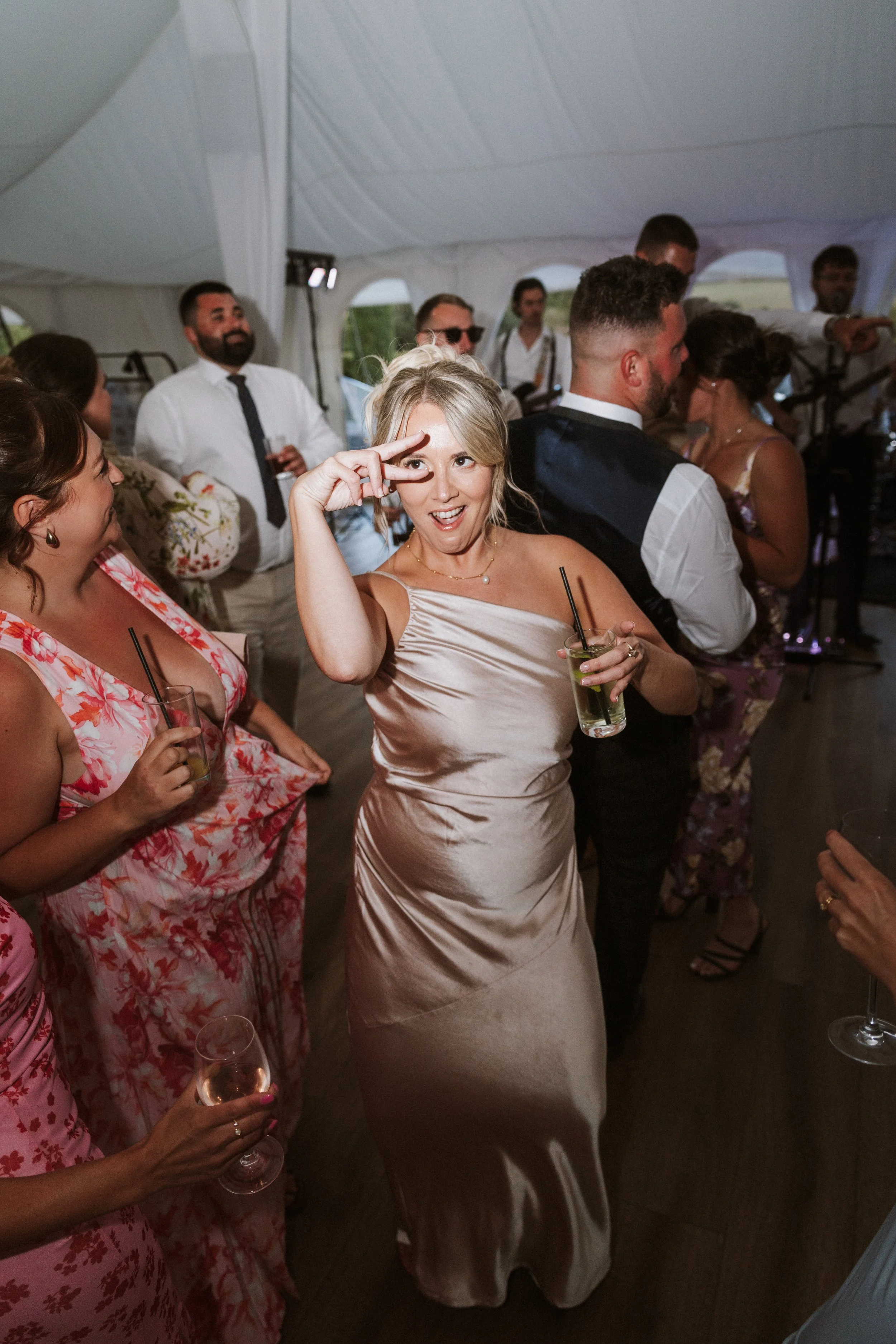 People are dancing and enjoying drinks at a wedding reception inside a large white event tent.