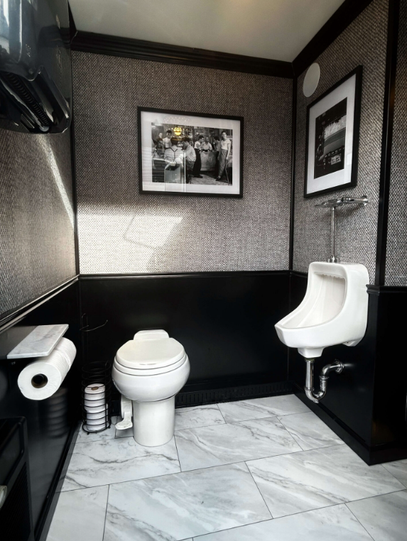 A black and white tiled restroom with a urinal, a toilet, and framed photos on the wall.