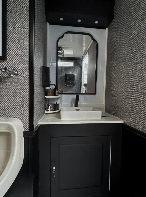 Bathroom with a white vessel sink, countertop, large mirror, black cabinet, and dark and textured wallpaper.